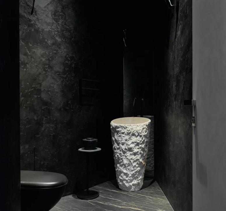 There's also a powder room with a black toilet and walls, a sculptural white stone sink and a little table