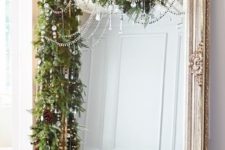 12 a lush evergreen garland with pinecones and crystals plus bead covers the large mirror bringing a strong Christmas feel to the space