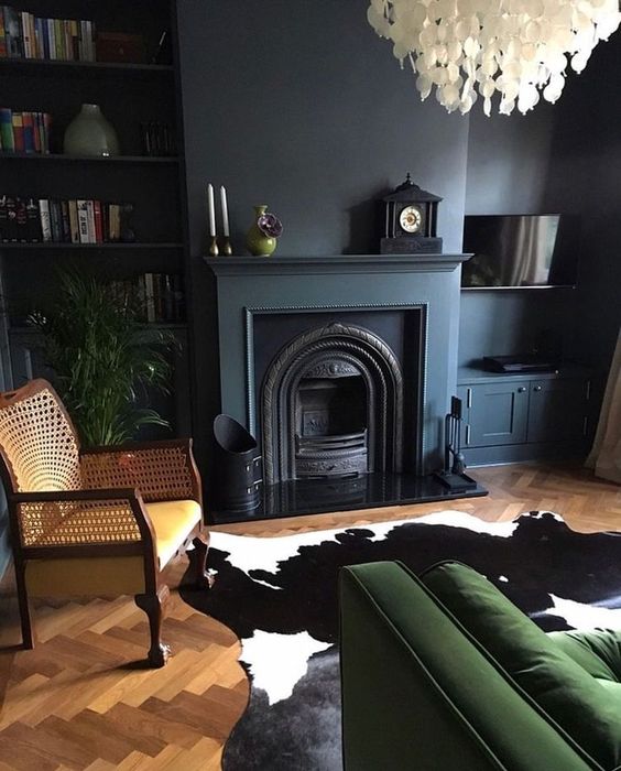 a dark toned living room with graphite grey walls, a green sofa, a rattan chair and a quirky seashell chandelier