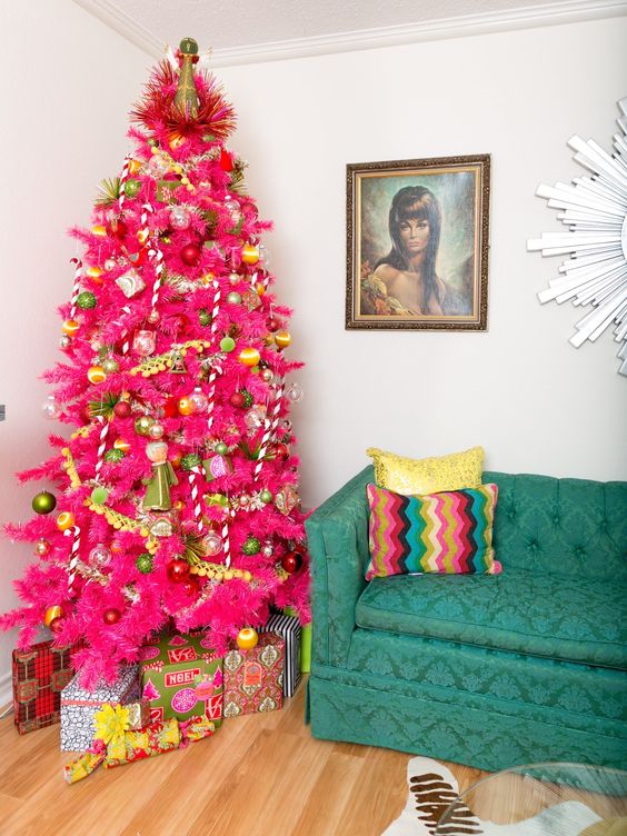 a hot pink Christmas tree with green and gold ornaments, pompom garlands and a quirky topper