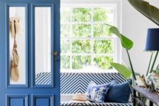 27 a stylish entryway dotted with classic blue – a door, a lamp, pillows, a striped upholstered bench and patterned pot