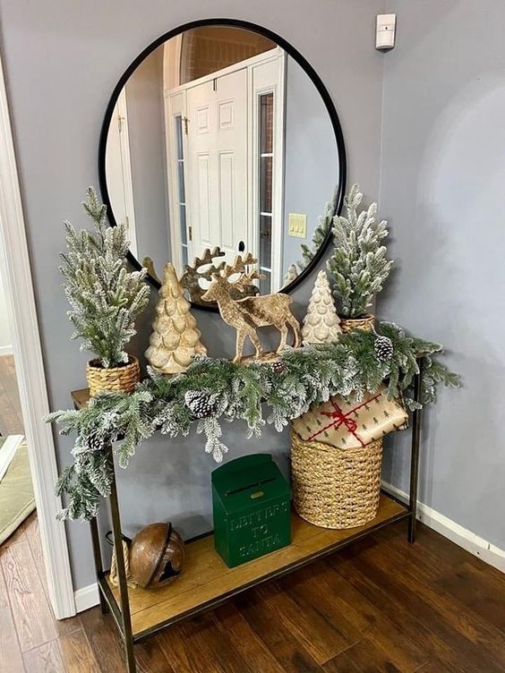 a Christmas console styled with potted flocked trees in baskets, evergreens and pinecones and faux trees and deer