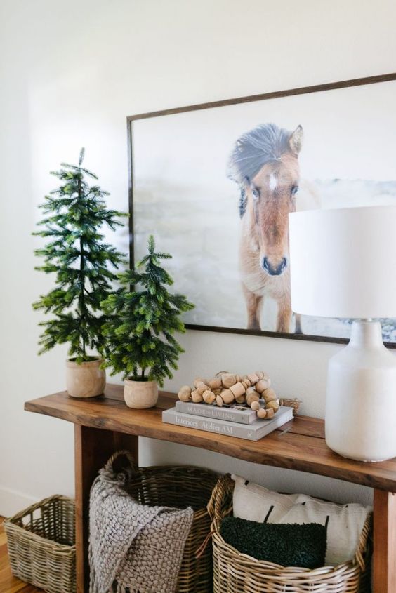 a duo of Christmas trees in planters, books and wooden beads, a table lamp for styling a console table