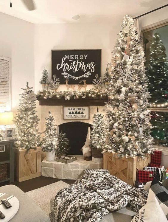 a farmhouse living room with multiple flocked Christmas trees with lights, pinecones, snowflakes and ribbons