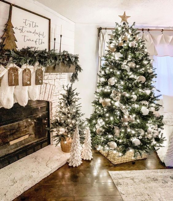 a large Christmas tree with white ornaments and lights and a smaller one in a basket are a cool combo for a farmhouse space