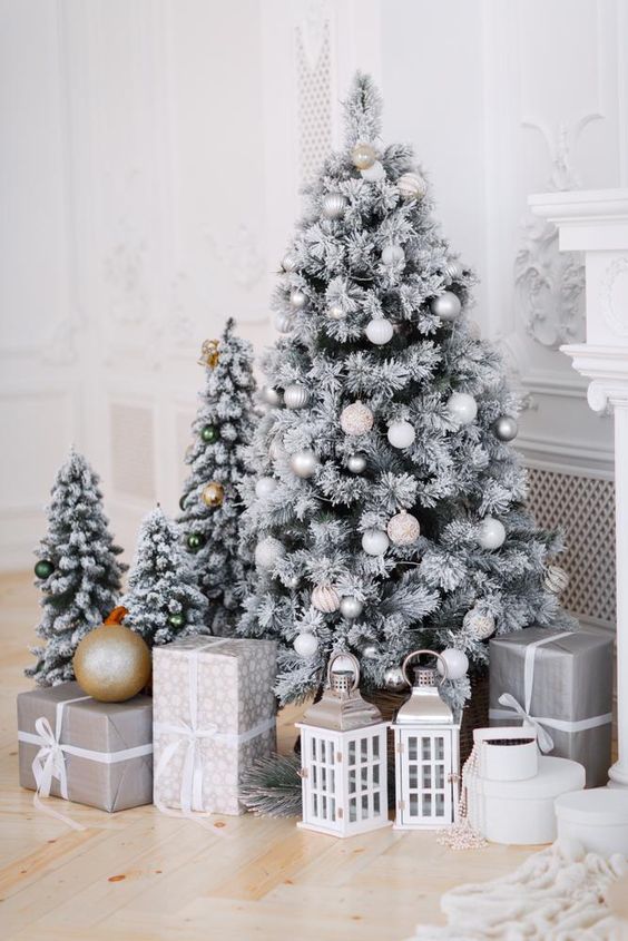 multiple flocked Christmas trees with metallic and white ornaments, lanterns and gift boxes are amazing