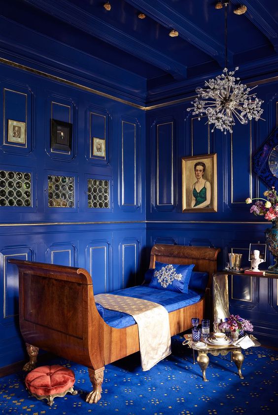 a bold purple-blue space with molding, an exquisite chandelier, a unique wooden daybed and artworks
