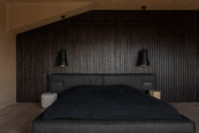 04 The bedroom is dark and soothing, with a wood clad wall, an upholstered dark bed and wall sconces