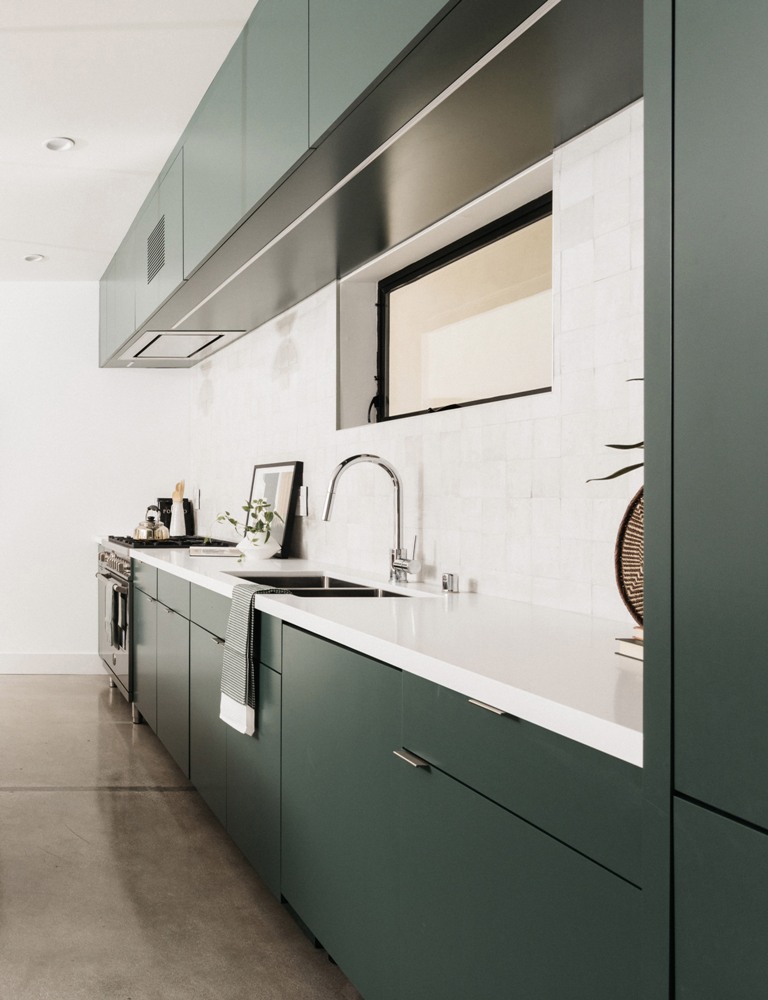 The kitchen is designed in dark green and white, with a chic tile backsplash and a matching white countertop The kitchen is designed in dark green and white, with a chic tile backsplash and a matching white countertop