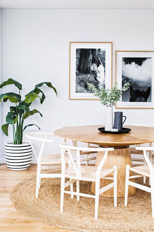 a chic coastal dining room with a wooden round table, a jute rug and lots of greenery