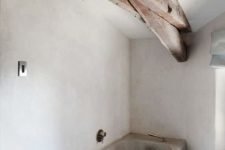 16 a concrete bathroom with white walls and a grey bathtub plus wooden beams on the ceiling
