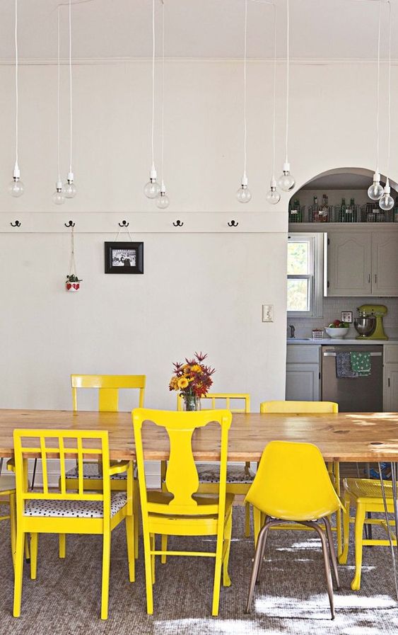 a dining room with a long wooden table and a number of mismatching chairs done in the same shade of yellow