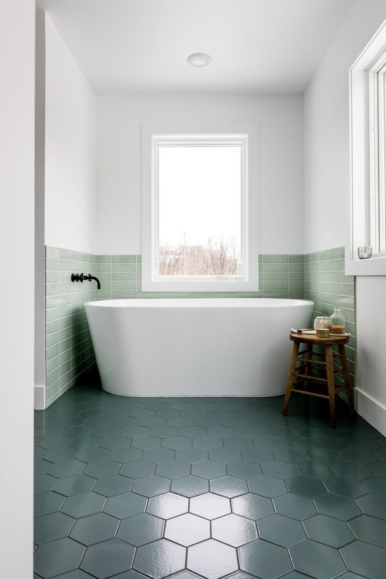 a contemporary bathroom with a bathtub niche covered with green tiles that match dark green floors
