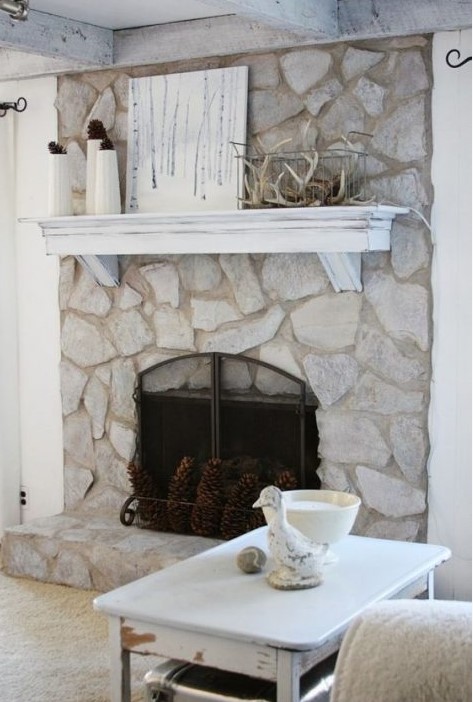a beautiful whitewashed stone fireplace with pinecones, a whitewashed mantel with antlers and pinecones for a woodland feel