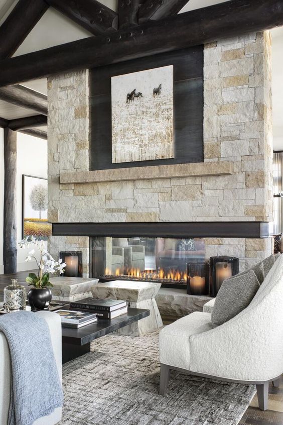 a chalet living room with stone stools, a low marble coffee table and seating furniture plus an amazing double-sided stone fireplace