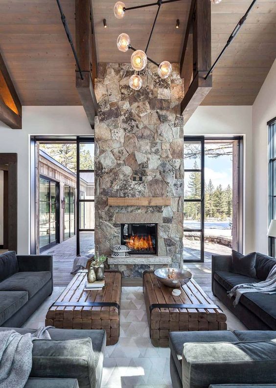 a chic contemporary cabin space with dark furniture, wood slab tables and a spectacular stone fireplace with a wooden mantel