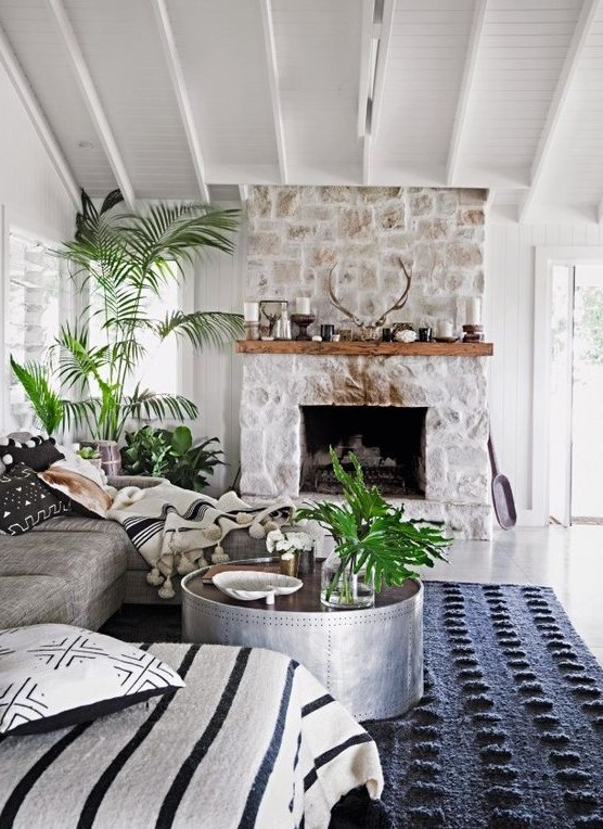 a chic monochromatic living room with a whitewashed stone fireplace, a wooden mantel with candles and antlers and potted plants