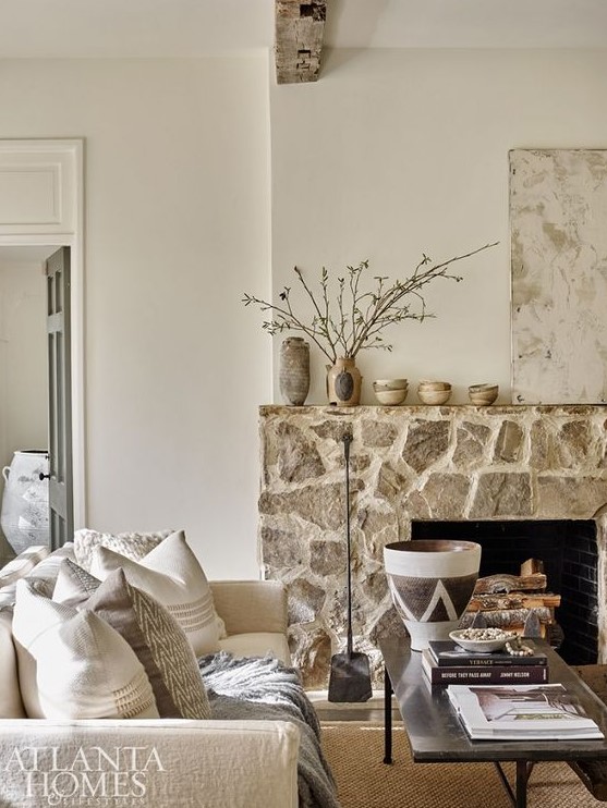 a chic neutral living room with a rough stone fireplace and neutral furniture, blooming branches that brings warmth here