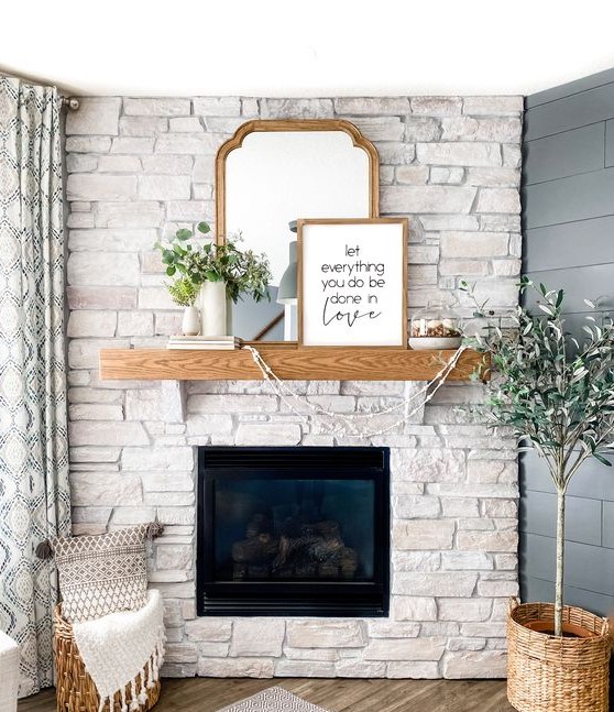 a chic whitewashed stone fireplace with a wooden mantel, askets and greenery in vases plus artworks on the mantel