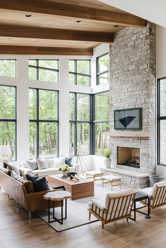 a clean and modern double-height living room with a grey stone fireplace and a wooden mantel as a centerpiece