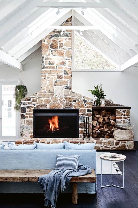 a coastal living room with a stone clad fireplace, a blue sofa, a bench, a side table and some greenery is wow