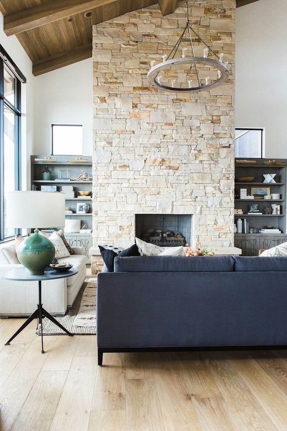 a contemporary living room in neutrals, with a double-height ceiling, a stone fireplace that warms up the space