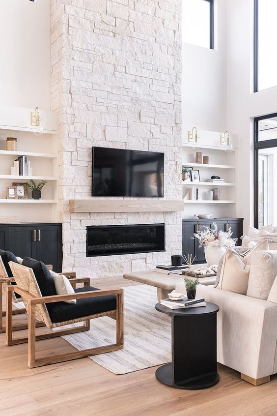 a contrasting living room with a stone fireplace, shelves and built-in cabinets, a white sofa, black chairs, a black side table