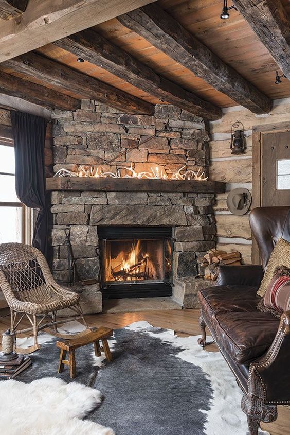 a dak cabin living room with a stone fireplace, antlers on the mantel, layered rugs and wicker and leather furniture