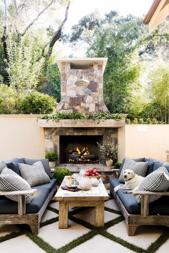 a fantastic rustic terrace with a stone fireplace, rough wood sofas and a wooden table, greenery and blooms and grass is wow