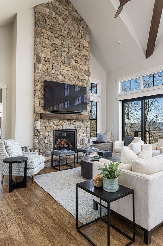 a modern chalet living room with a stone fireplace, neutral seating furniture, a coffee table and stools