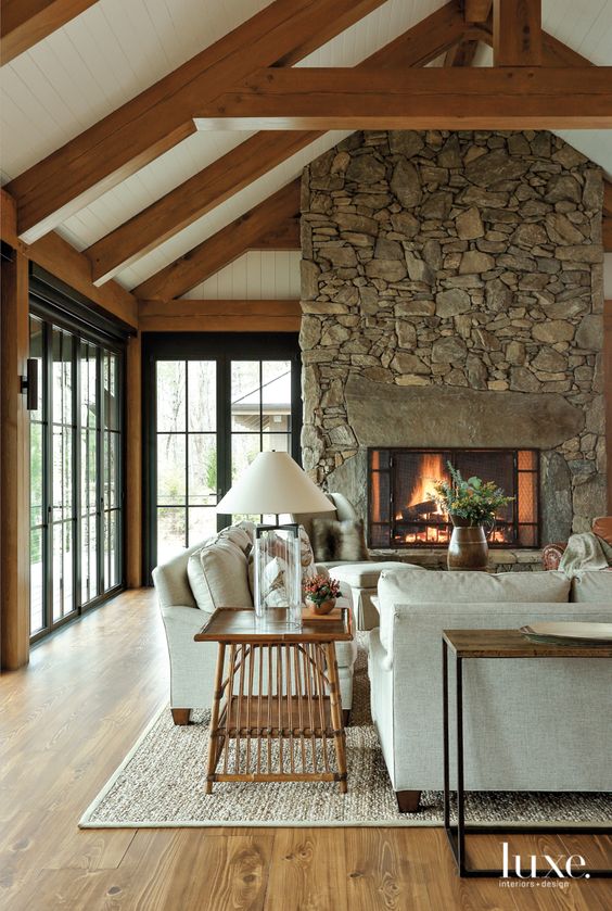 a modern chalet living room with a stone fireplace, neutral seating furniture, a stained side table and a console one