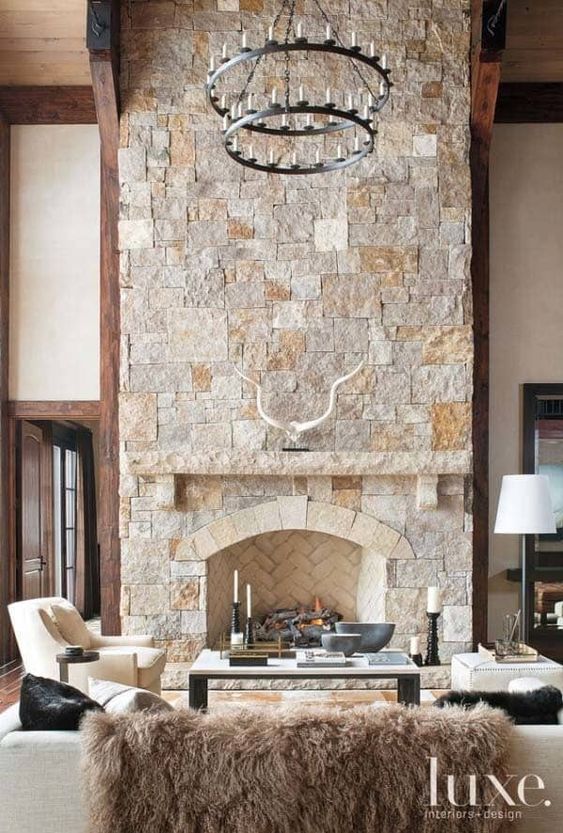 a modern chalet living room with a stone fireplace, neutral seating furniture, a tiered metal chandelier