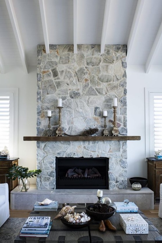 a modern coastal living room warmed up with a whitewashed stone fireplace, a rough wooden mantel and wooden candle holders