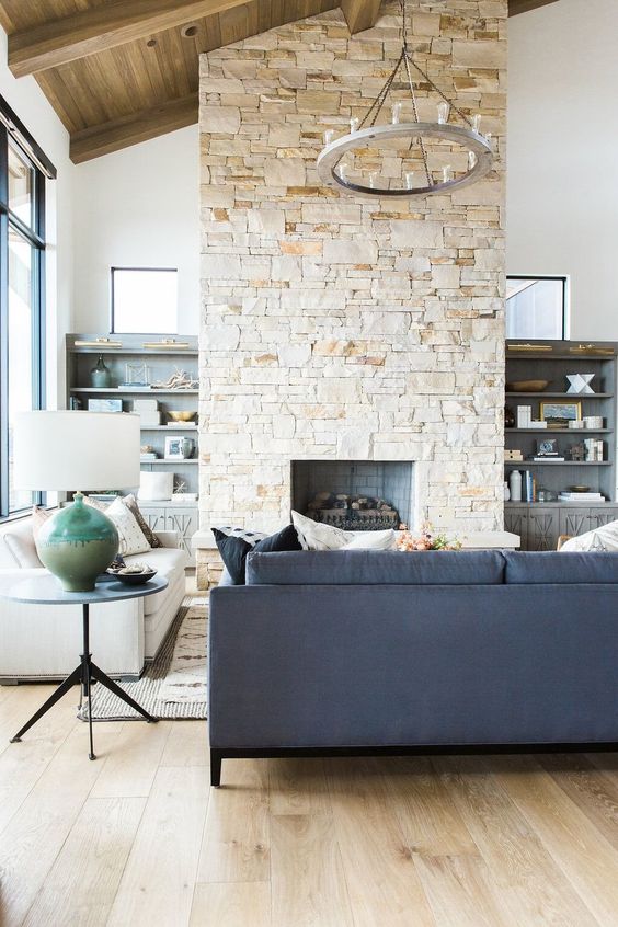 a modern farmhouse living room with a navy sofa, a white one, a coffee table, a stone fireplace and a chandelier