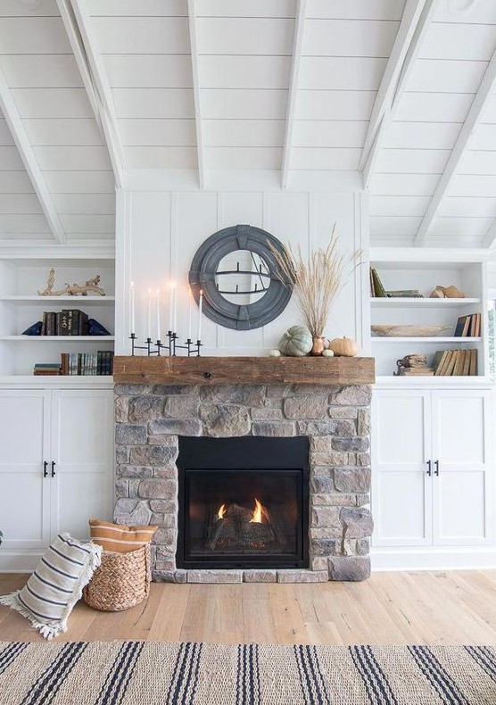 a modern farmhouse living room with a stone fireplace, a wooden mantel, candles and pumpkins and some wheat in a vase