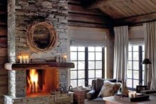 a moody neutral living room with a grey stone fireplace, vintage furniture, faux fur rugs and blankets and candles