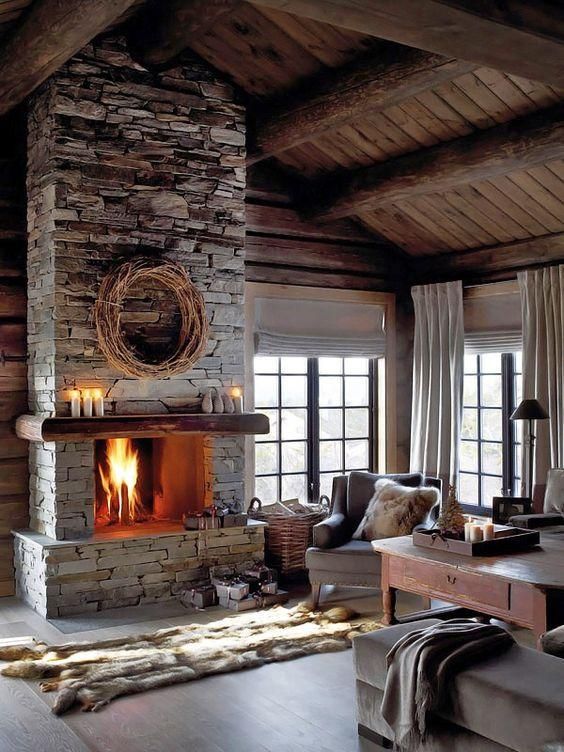 a moody neutral living room with a grey stone fireplace, vintage furniture, faux fur rugs and blankets and candles