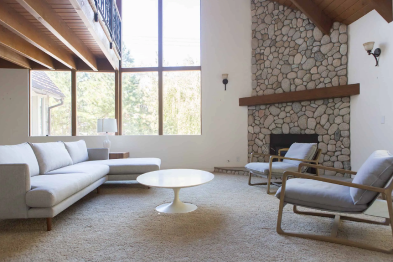 a neutral and clean minimalist space with a qurky corner stone clad fireplace with a dark stained wooden mantel