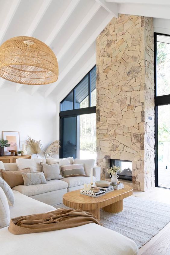 a neutral boho living room with a stone fireplace, a neutral sectional a low coffee table and a woven pendant lamp