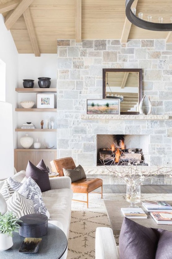 a neutral farmhouse living room with a stone fireplace, a wooden mantel, artworks and a mirror that becomes a centerpiece here