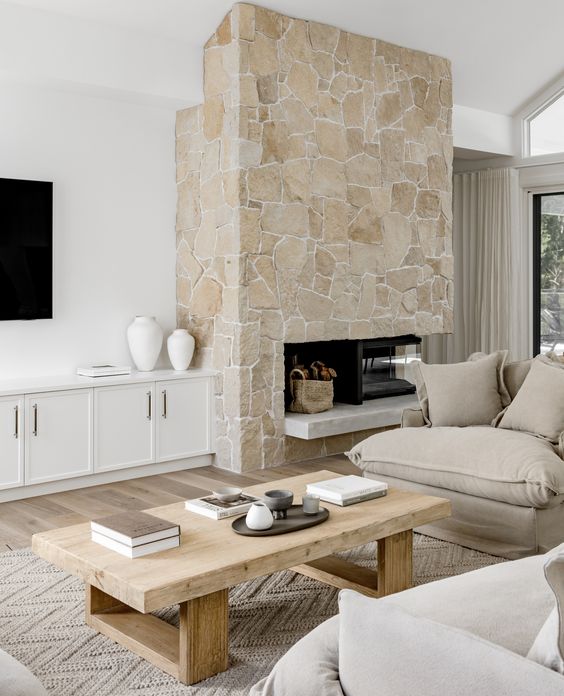 a neutral living room with a stone fireplace, neutral seating furniture, a low coffee table and white built-in cabinets