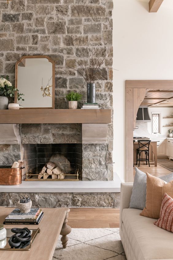 a neutral living room with a stone fireplace, neutral seating furniture, a low coffee table, potted greenery