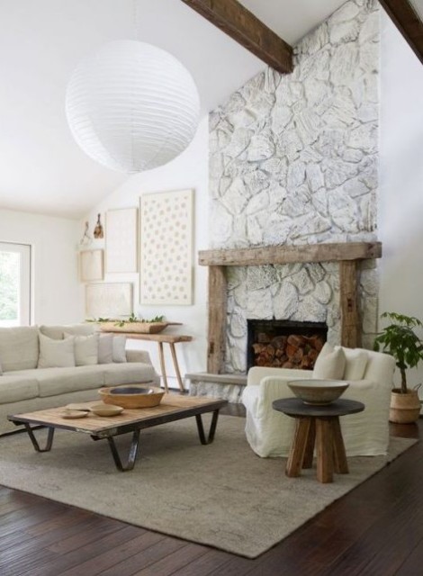 a neutral living room with a whitewashed stone fireplace, a wooden mantel and furniture, a gallery wall and a potted plant