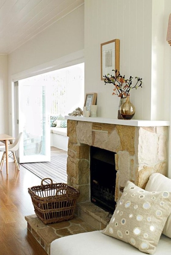 a neutral stone fireplace with a basket for firewood and a white mantel with candles, vases and blooms makes the space cozy and chic