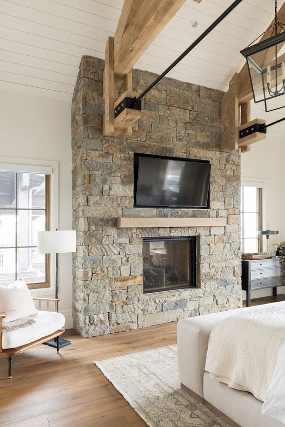 a ranch bedroom done with a rough stone fireplace with a wooden mantel matching the beams is a lovely and welcoming space