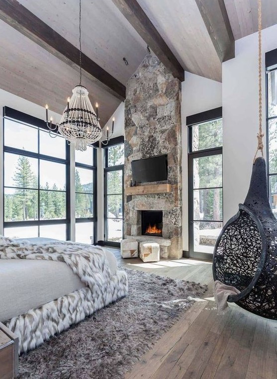 a refined chalet bedroom with wooden beams, a stone fireplace with ottomans and a pendant cocoon chair