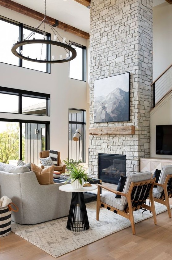 a refined ranch living room with a stone fireplace, wooden mantel and an artwork plus chic grey furniture