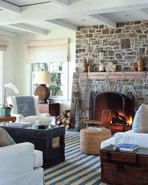 a vintage coastal living room with a stone fireplace, a chest, a jute pouf, some seating furniture and some decor and accessories