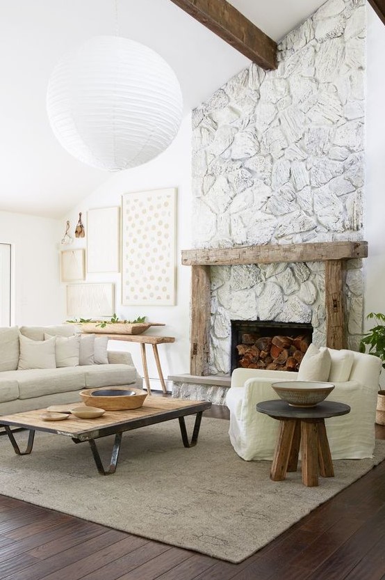 a whitewashed stone fireplace with a rough wood mantel, firewood inside brings a cozy farmhouse feel to the room