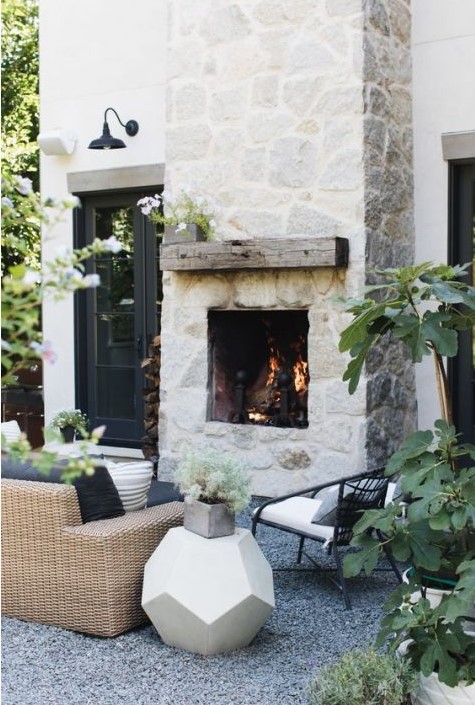 a whitewashed stone fireplace with a rough wooden mantel is a centerpiece of this chic outdoor space